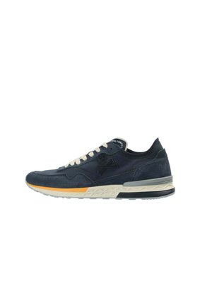 Zapatilla baja azul marino con cordones blancos, parte superior de ante y malla, emblema de calavera en el lateral y suela texturizada blanca y amarilla.