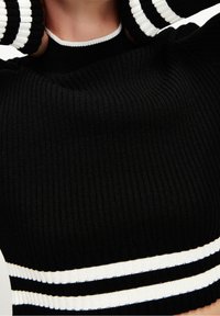 Haut en tricot noir à côtes avec un col rond et des accents rayés en blanc et bleu au bas et aux manches. La texture est douce et ajustée.