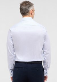 Camicia a maniche lunghe a strisce blu chiaro con colletto a punta e polsini con bottone, abbinata a pantaloni navy con cintura intrecciata.