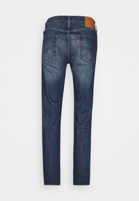 Mörkblå denimjeans med rak passform, med två bakfickor, synlig sömnad och en brun läderetikett på midjan.