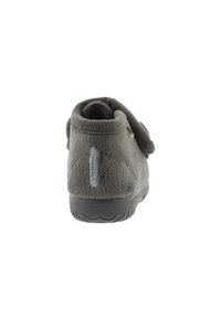 Pantofole grigie in peluche con design arrotondato, cinturino in velcro e suola in gomma con texture. Il retro presenta una cucitura verticale e un dettaglio con il logo.