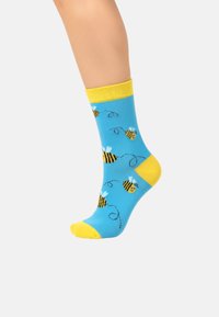 Baumwollsocken mit einem hellblauen Hintergrund, gelben Akzenten und einem Bienenmuster, das schwarze und gelbe Streifen mit dekorativen Wirbeln zeigt.