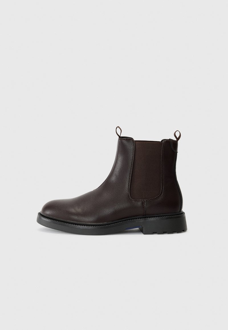 Botte en cuir marron à cheville avec des panneaux élastiques sur les côtés, des poignées de tirage et une semelle en caoutchouc noir dotée d'un motif de crampons pour une meilleure adhérence.