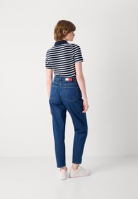 Stripet navy og hvit polo skjorte kombinert med høytlivs blå jeans. Modell som har på seg hvite sneakers med rosa detaljer, vist fra bak.