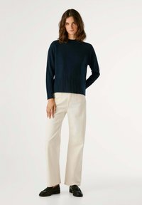 Marineblauw geribbeld sweater met lange mouwen, ontspannen pasvorm en gestructureerde onderzoom; gecombineerd met lichtbeige wijde broek en zwarte schoenen.