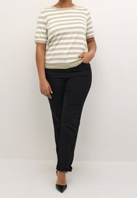 Top de punto a rayas en beige y blanco con mangas cortas, combinado con pantalones slim-fit negros y tacones negros de punta. Diseño y textura sencillos.