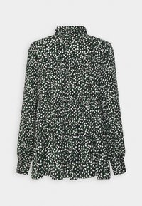 Chemise noire à manches longues avec un motif floral blanc et vert. Design à col avec des plis froncés sur le devant pour plus de texture.