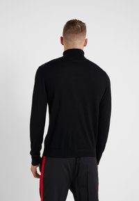Maglione nero a collo alto realizzato in tessuto a maglia fine, con maniche lunghe e un design aderente, caratterizzato da una texture liscia e privo di ornamenti.