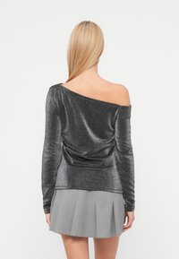 Λαμπερό γκρι τοπ έξω από τον ώμο με μακριά μανίκια, με σχεδιασμό draped και απαλή υφή, σε συνδυασμό με γκρι πλισέ φούστα.