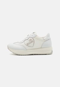 White leather sneaker with rounded toe, contrasting laces, and a heart logo featuring "LOVE MOSCHINO" in gray on the side. Rubber sole.