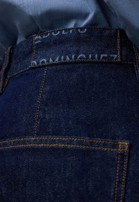 Jeans i mörkblå denim med kontrasterande orange sömmar, med en etikett sydd i midjebandet och en klassisk femfickorsdesign.