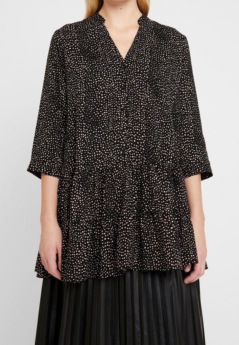 Czarna tunika z różowymi kropkami, dekoltem w kształcie v, rękawami o długości trzy czwarte, falbaną u dołu, wykonana z lekkiego materiału. Guziki z przodu.