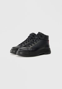 Baskets montantes noires en cuir texturé, avec un design à lacets, une semelle épaisse et un accent rouge à l'arrière.