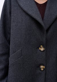 Donkergrijze wollen jas met een herringbone patroon, brede kraag, drie grote knopen en een zijzak.