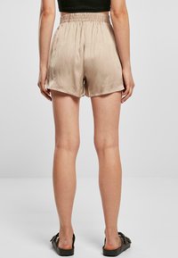 Shorts en satin beige clair avec une taille élastique, texture lisse et coupe décontractée, dotés d'un ourlet simple et d fentes latérales.