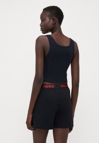 Svart linne med rundad halsringning, kombinerat med svarta shorts med en röd "HUGO" midjeresår. Slät текстur och figursydd design.