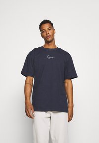 Camiseta de algodón azul marino con cuello redondo y mangas cortas, que presenta un diseño de logo blanco en el pecho. Textura suave, corte relajado.