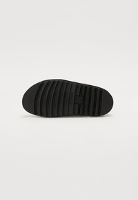 Suola di scarpa in gomma nera con superficie testurizzata, caratterizzata da scanalature orizzontali per migliorare la presa e una punta arrotondata. Branding minimale visibile.
