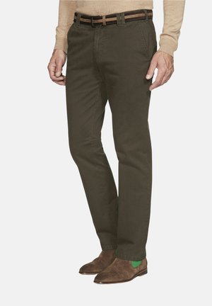 Man wearing olive green pants, brown suede shoes with green elastic sides, a beige sweater, and a two-tone brown belt.