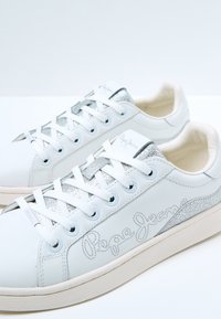 Sneakers en cuir blanc avec des accents argentés, un laçage texturé et une marque 'Pepe Jeans' sur le côté. Semelle en caoutchouc au design minimal.
