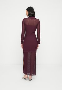 Lang burgunderfarget kjole med ribbet tekstur, lange ermer og sidespalter; har et gjennomsiktig øvre ryggdesign og en tettsittende silhuett.