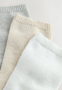 Three pairs of knitted socks in gray, beige, and white. Each features a ribbed cuff and soft, textured fabric with subtle variations.