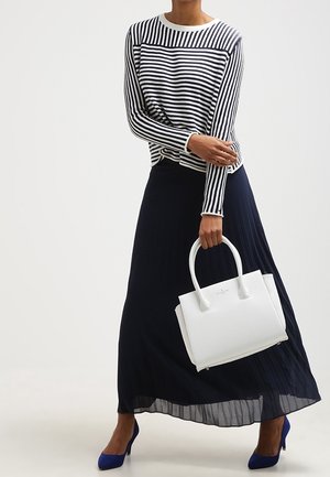 Witte gestructureerde handtas met een textuurafwerking, gecombineerd met een marineblauwe geplooide maxirok en een zwart-wit gestreept shirt met lange mouwen.