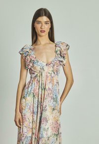 Blumiges Maxikleid in Pastellfarben mit Rüschensäumen, V-Ausschnitt und fließendem Stoff, der mit Mustern von pinken, blauen und gelben Blumen versehen ist.