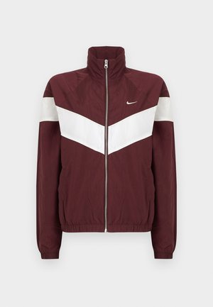Bordo vjetrovka s bijelim chevron prugama, visokim ovratom, prednjim zatvaračem, elastičnim manžetama i donjim rubom; Nike logo na lijevoj strani prsiju.