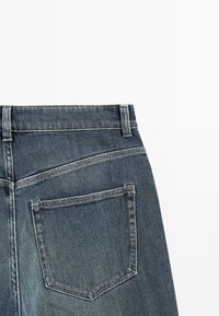 Džíny z denimu s vysokým pasem, v tmavě modré barvě. Obsahují dvojité šití, jednu zadní kapsu a rovný střih na spodním lemu.