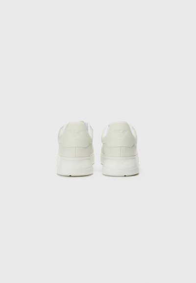 Baskets blanches avec une finition lisse, un talon rond et une collerette rembourrée. Détail de logo subtil gaufré sur le talon. Design minimaliste.