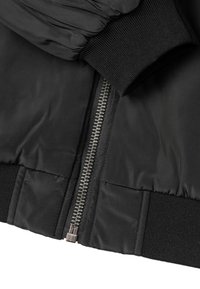La giacca bomber nera presenta un tessuto liscio e lucido, polsini a coste e una zip metallica. Il design include sezioni trapuntate per aggiungere texture.
