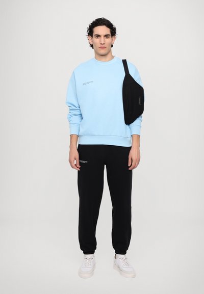 Light blue sweatshirt with text detail, black joggers with side pockets, and white sneakers, worn with a black crossbody bag.
