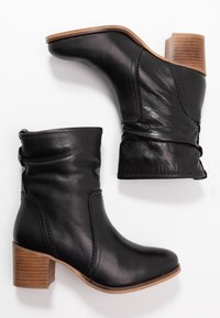 Bottes basses en cuir noir à design plissé, talons en bois empilés, et détails de couture visibles. Texture lisse avec une finition brillante.