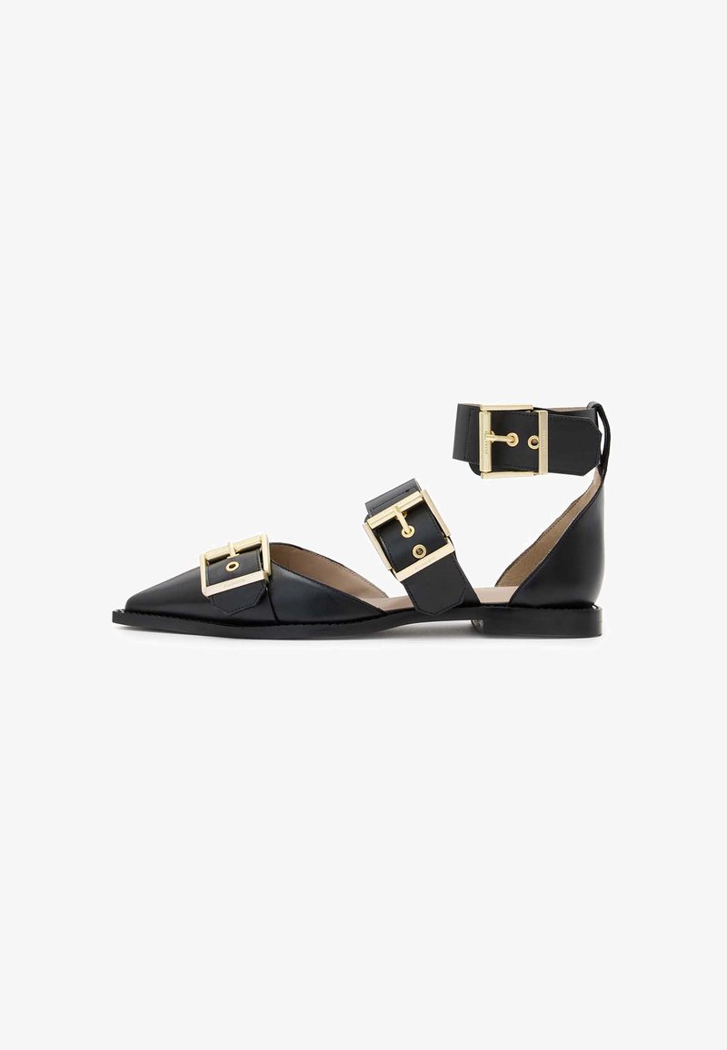 Black leather flat sandals featuring a pointed toe, double buckle accents, and ankle straps. Smooth texture with gold-tone hardware details.