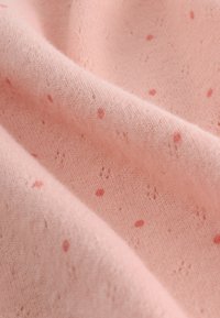 Hele roosa kangas pehme tekstuuriga, millel on väikesed punaka värvusega täpid ja õrn kootud muster. Sile kergelt läikiv langevus.