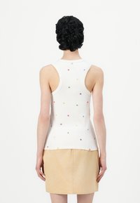Witte geribbelde tanktop met kleurrijke bloemenborduursels. De achterkant is gekenmerkt door een ronde halslijn en een mouwloos ontwerp.