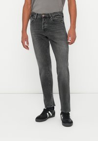 Jeans de denim gris con corte ajustado, que cuentan con cinco bolsillos, un ligero desvanecimiento y un cierre de botón, combinados con zapatillas negras.