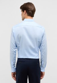 Lichtblauw overhemd met lange mouwen en een soepele textuur, met knoopmanchetten en een klassieke kraag, gecombineerd met een marineblauwe broek.