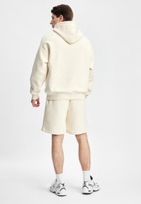 Kremfarget hettegenser med myk tekstur og stor hette, kombinert med matchende shorts. Enkle joggesko fullfører antrekket.