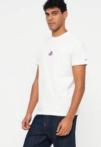 Λευκό βαμβακερό μπλουζάκι με κοντό μανίκι που διαθέτει ένα μικρό κεντημένο λογότυπο σε κόκκινο και μπλε στην περιοχή του στήθους, με κλασικό λαιμόκοψη.