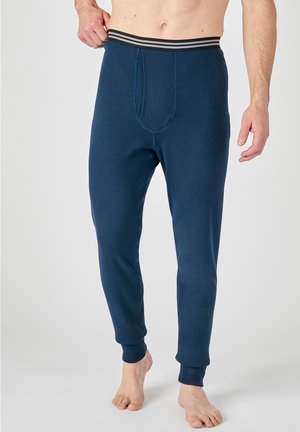 Man wearing dark blue thermal pants with striped elastic waistband standing barefoot against a plain background.