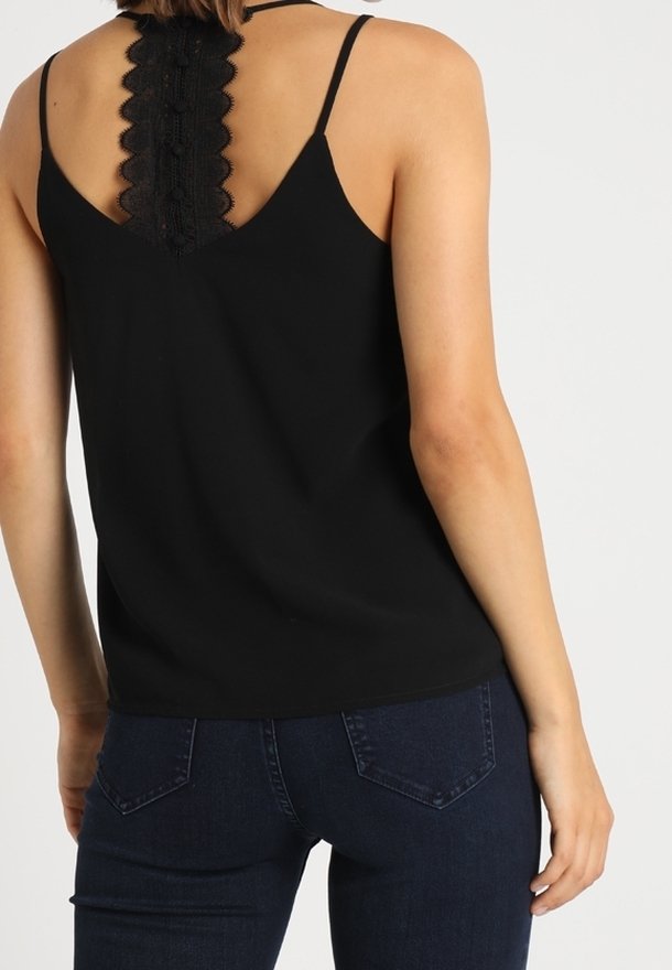 Svart ärmlös topp med spetsdetaljer på baksidan, med smala axelband och en avslappnad passform, tillsammans med mörkblå jeans.