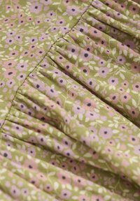 Fabric with a green background featuring small pink and purple floral patterns. Includes gathered detailing and a textured surface.