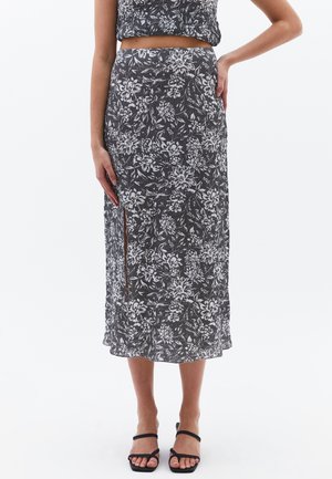 Schwarz-weiße, floral gemusterte Midi-Rock. Mit einem seitlichen Schlitz, leichtem Stoff und tailliertem Bund. Wird mit schwarzen Riemchen-Sandalen kombiniert.