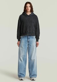 Felpa nera corta con finitura testurizzata e cappuccio con lacci, abbinata a jeans in denim azzurri a gamba larga.