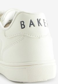 Zapatilla blanca de cuero con cuello acolchado, detalle en relieve de "BAKER", suela de goma texturizada y superficie suave con costuras accentuadas.