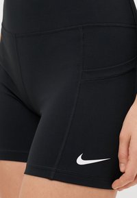 Calções atléticos pretos feitos de um tecido elástico com uma textura suave. Inclui um logótipo Nike branco e detalhes de costura discretos.