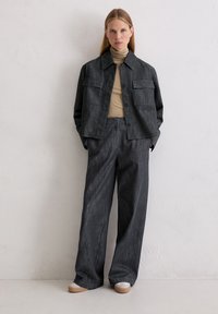 Ciemna kurtka dżinsowa z dwoma kieszeniami na piersi, zestawiona z pasującymi spodniami o szerokich nogawkach. Pod spodem beżowy golf. Miękka tekstura, luźny krój.