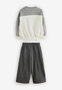 Siva in krem dvodelni komplet, ki vključuje polarno pulover s sivim zgornjim delom in teksturiranim kremnim dnom, v kombinaciji s temnosivimi kratkimi hlačami.